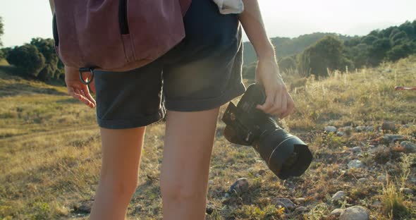 Female Travel Blogger in Mountains with Backpack Hold Photo Camera on Sunset alt