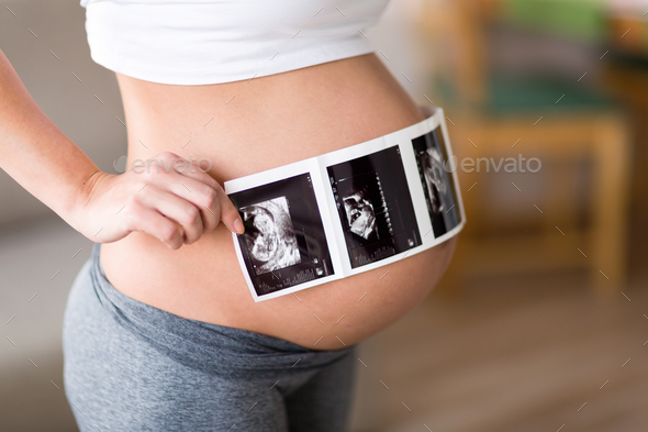 Pregnant woman holding ultrasound photo on belly Stock Photo by nd3000