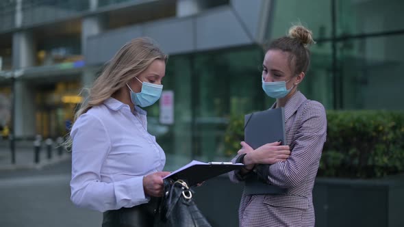 Two young business women wearing medical masks meet on the street to communicate alt