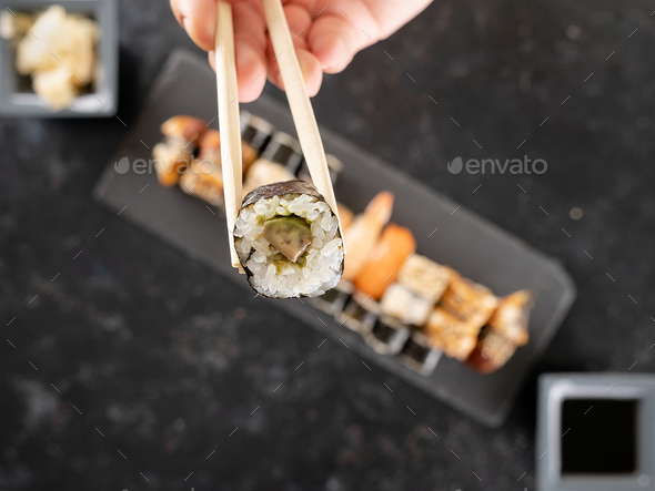 Chopstick with a sushi in focus and a mix of sushi on dark stone - Stock Photo - Images
