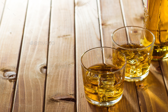 Glass of alcoholic drink with ice cubes on wooden table. Stock Photo by jirkaejc