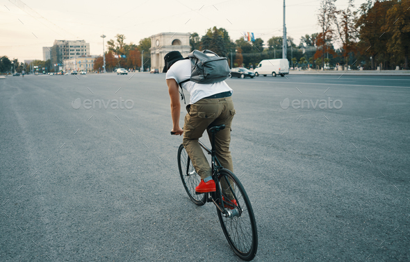Young modern man cycling on a classic bike on the city road with Stock Photo by arthurhidden