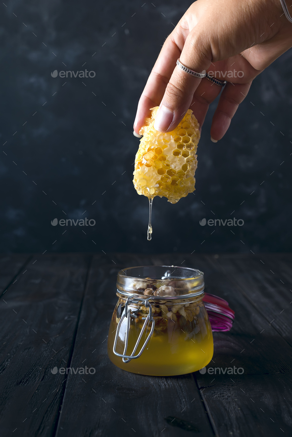 The girl\'s hands hold a piece of honeycomb, from which honey flows into the jar Stock Photo by lyulkamazur