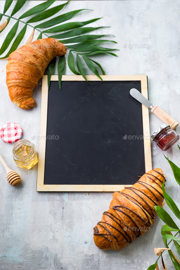 croissants, honey, jam and berries on the trip. Background of a chalkboard, palm leaf