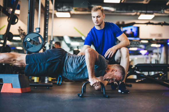 Young man helping senior man in a workout. Stock Photo by photocreo