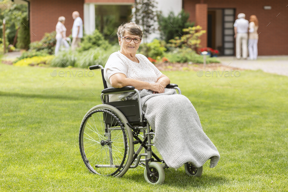Happy disabled elderly woman in a wheelchair on green grass duri
