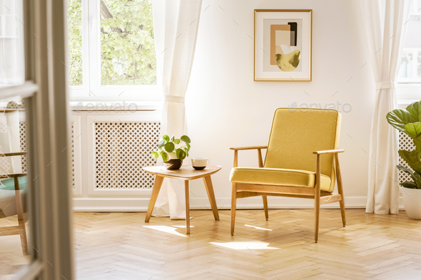 A retro, yellow armchair and a wooden table in a beautiful, sunn - Stock Photo - Images