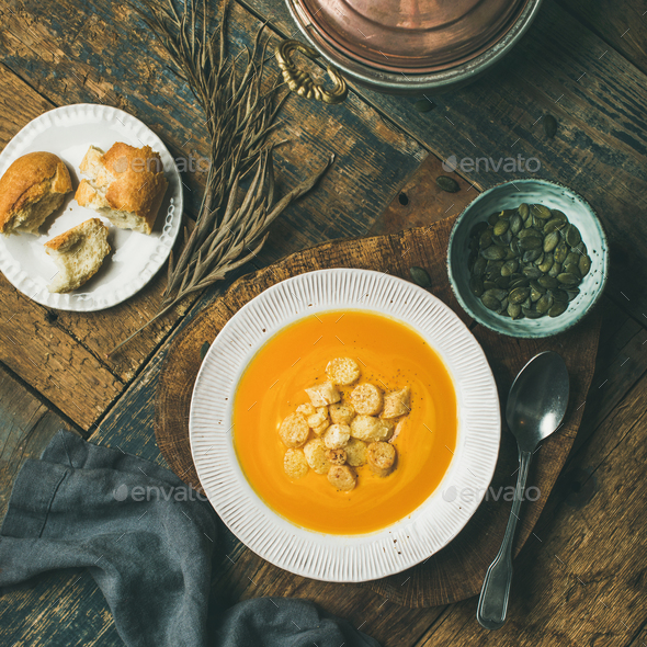 Warming pumpkin cream soup with croutons and seeds on board - Stock Photo - Images