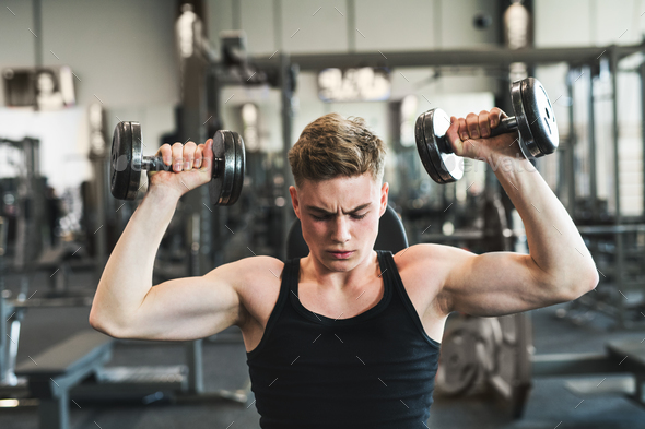 Young fit man in gym exercising with dumbbells. Stock Photo by halfpoint