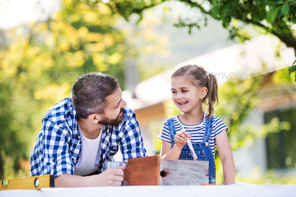 Father with a small daughter outside, painting wooden birdhouse.