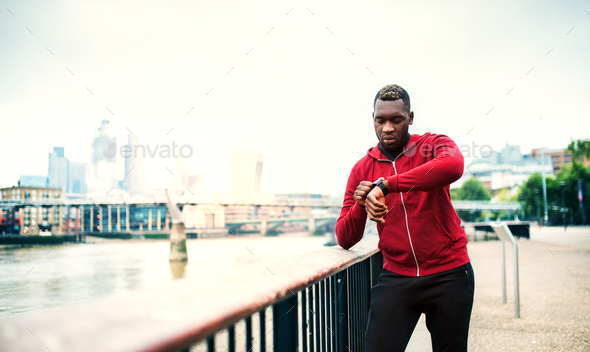 Young sporty black man runner on the bridge outside in a city, setting smartwatch. Stock Photo by halfpoint