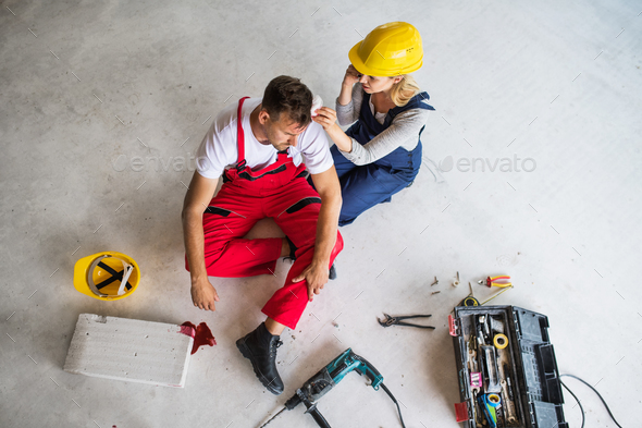 A woman with smartphone helping man worker after an accident at the construction site. Stock Photo by halfpoint