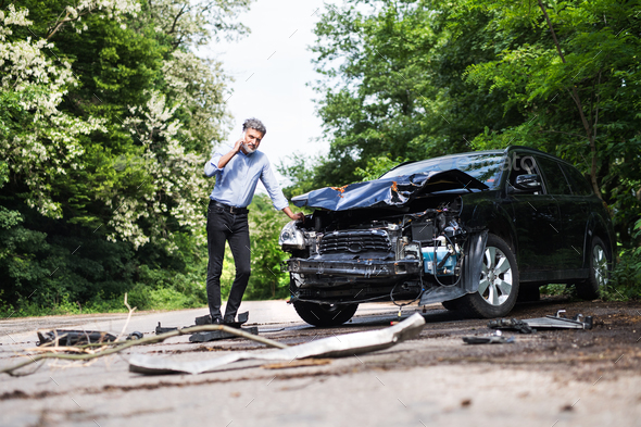 Mature man standing by the car, making a phone call after a car accident. Stock Photo by halfpoint
