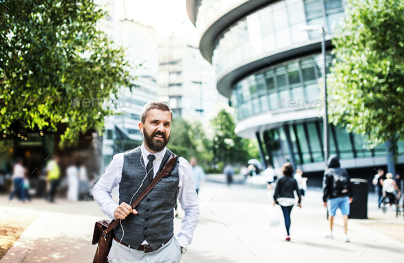 Hipster businessman with earphones walking on the street in London. Stock Photo by halfpoint