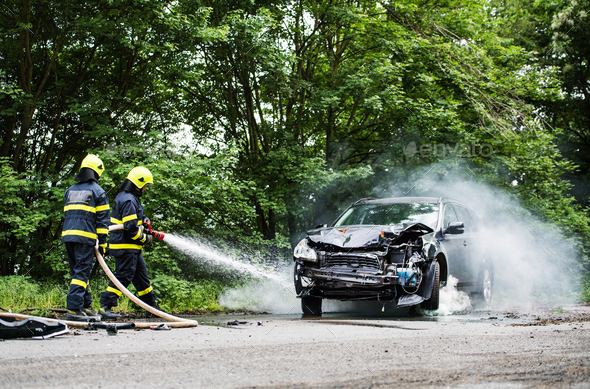 Two firefighters extinguishing a burning car after an accident. - Stock Photo - Images
