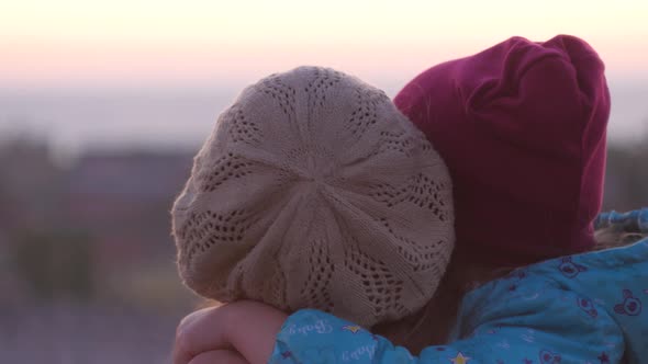 Mother and daughter standing on evening city lanscape. A little girl hugging and kissing mom alt