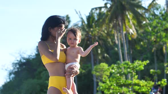 A Filipino Mother with Half Caucasian Baby Standing at the Beach on Vacation