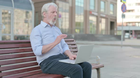 Old Man with Neck Pain Using Laptop While Sitting Outdoor on Bench alt