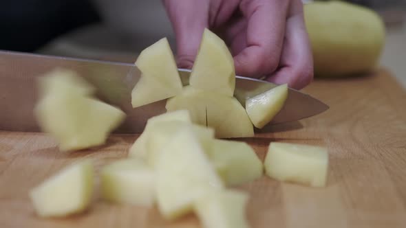 The chef's hand is cutting potatoes into slices with a knife on a cutting board.