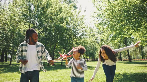 Cute Black Girl and Her Parents are Playing in the Park with a Red Plane alt