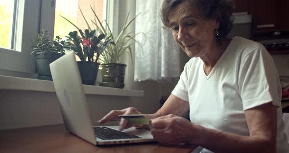Elderly Woman Holding Credit Card and Typing on Laptop