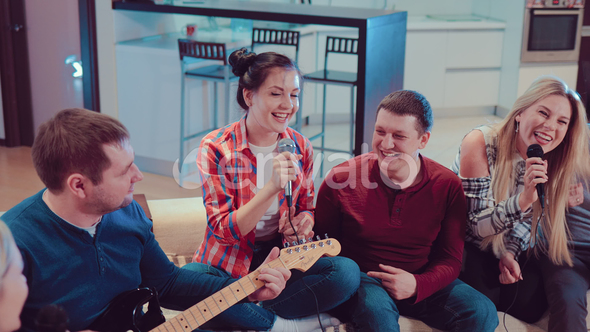 Group of Young Hipster Friends Sitting on the Couch and Playing Guitar and Singing Songs alt
