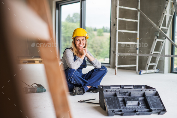 Young woman worker sitting on the floor on the construction site. Stock Photo by halfpoint