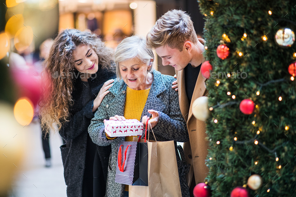 A young couple giving a present to grandmother in shopping center at Christmas. Stock Photo by halfpoint