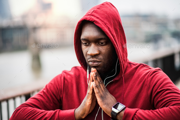 A close-up of black man runner with earphones and hood on his head in a city. Copy space. Stock Photo by halfpoint