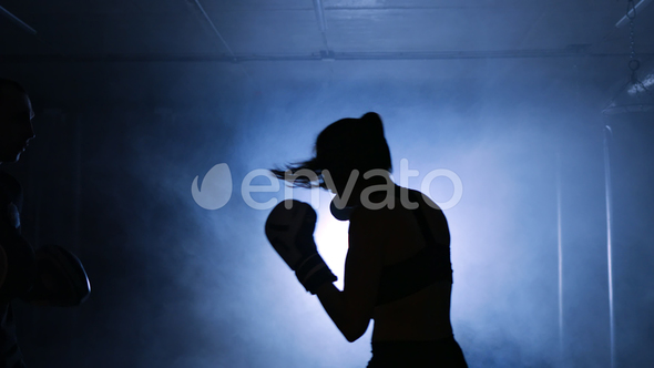 Young Woman Training with a Coach in a Boxing Club in a Smoky Gym Silhouette alt