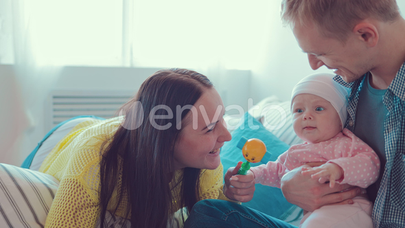 Child sits on his father's lap, and mom kisses her baby