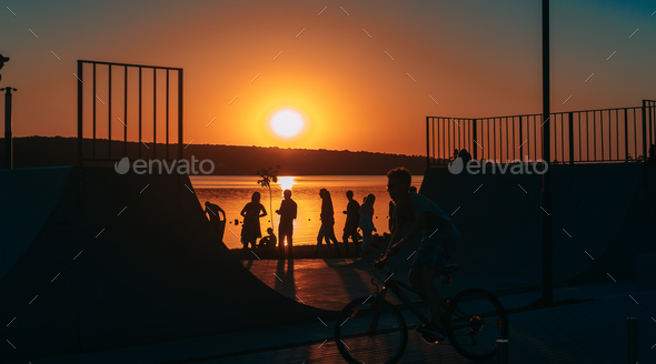 people are resting on a sports field by the river bank Stock Photo by simbiothy
