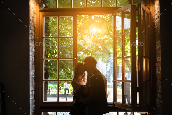 Young couple in love standing by the window Stock Photo by simbiothy