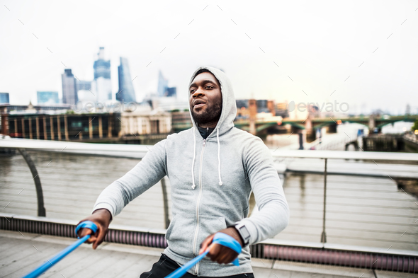 Young black sportsman exercising with elastic rubber bands in London.