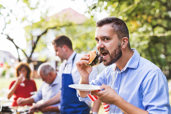 A mature man with family and friends cooking food on a barbecue party. Stock Photo by halfpoint