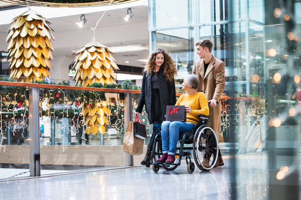 A grandmother in wheelchair and teenage grandchildren in shopping center at Christmas. Stock Photo by halfpoint
