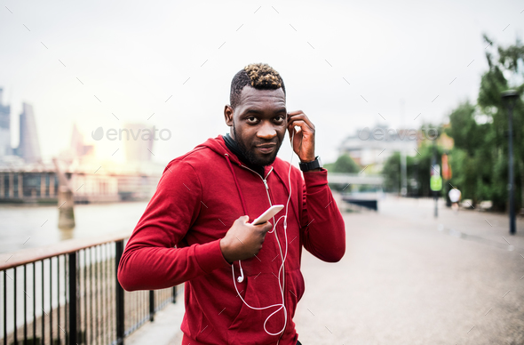 Young sporty black man runner on the bridge outside in a city, using smartphone. Stock Photo by halfpoint
