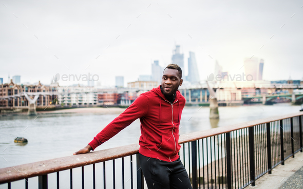 Young sporty black man runner on the bridge outside in a city, resting. Stock Photo by halfpoint