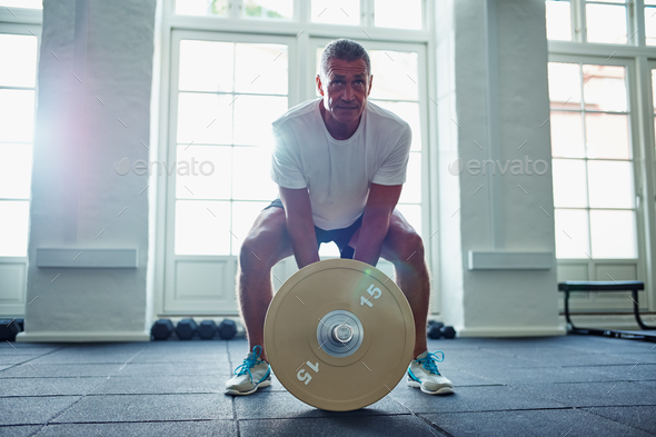 Mature man in sportswear lifting weights alone in a gym Stock Photo by UberImages