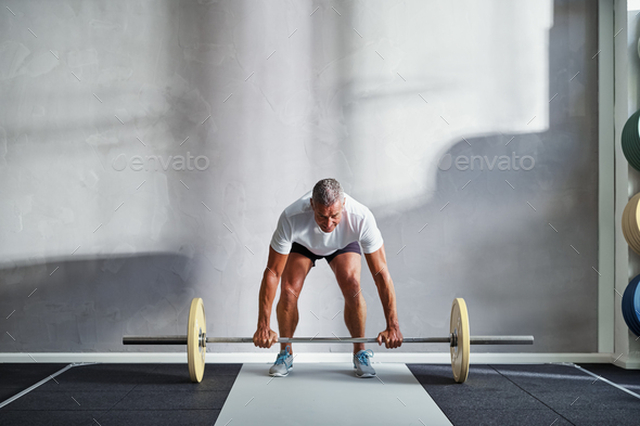 Fit mature man lifting weights alone in a gym Stock Photo by UberImages