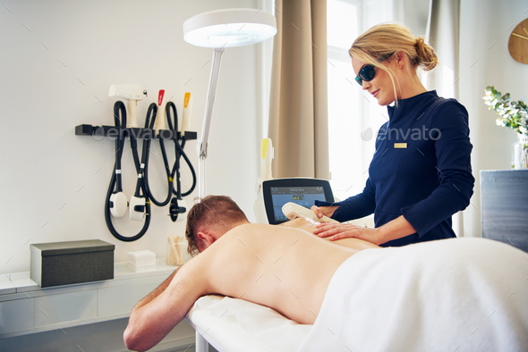 Beautician performing laser hair removal on a male client Stock Photo by UberImages