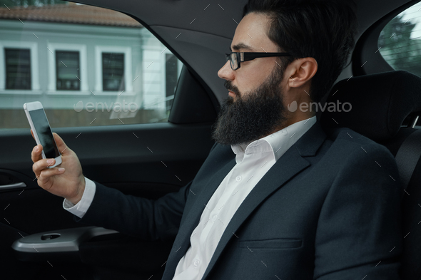 A businessman while traveling by car in the back seat using a sm - Stock Photo - Images