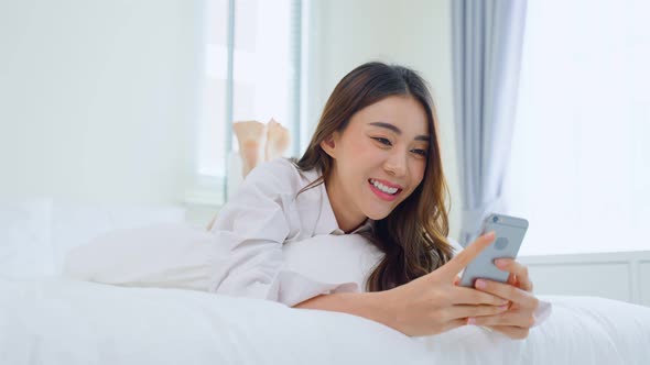 Asian attractive woman lying down on bed, use mobile phone chat in bedroom at home in morning. alt