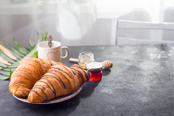 freshly baked croissant and cup of coffee decorated with chocolate sauce and palm leav Stock Photo by lyulkamazur