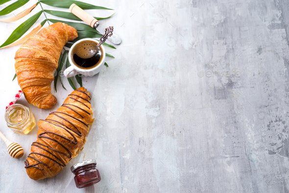 freshly baked croissant and cup of coffee decorated with chocolate sauce and palm leave Stock Photo by lyulkamazur