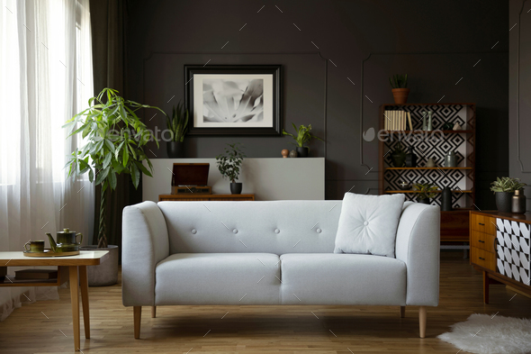 Wooden table next to grey sofa in dark living room interior with Stock Photo by bialasiewicz