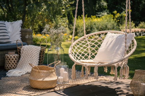 A beige string swing with a pillow on a patio. Wicker baskets, a Stock Photo by bialasiewicz