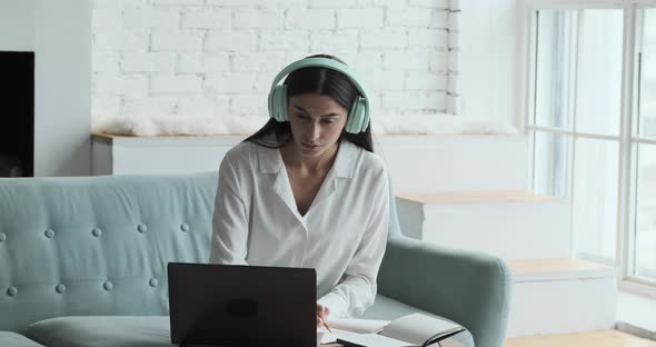 Young Woman Writing in Notepad and Looking at Laptop with Tutorial alt