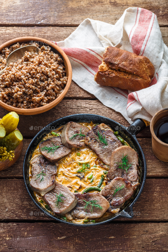Beef tongue in cast iron skillet with cream sauce, rustic style. Stock Photo by fazeful