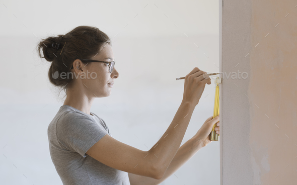 Woman doing a home renovation and measuring walls with a ruler